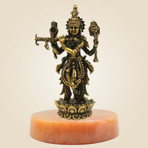 Bronze statue of a deity on a pink stone base against a beige background