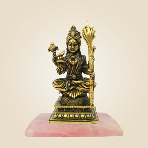 Gold-colored statue of a deity on a pink base against a beige background
