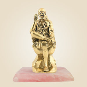 Gold statue of a seated figure on a pink base against a beige background