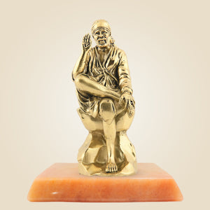 Gold statue of a seated figure on an orange base against a beige background