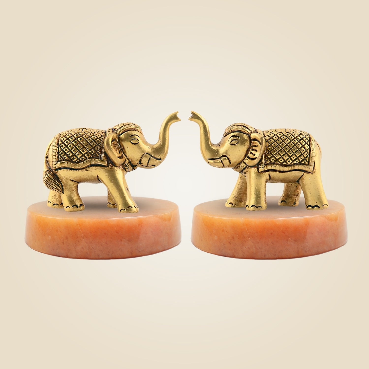 Two gold elephant figurines on red bases against a beige background