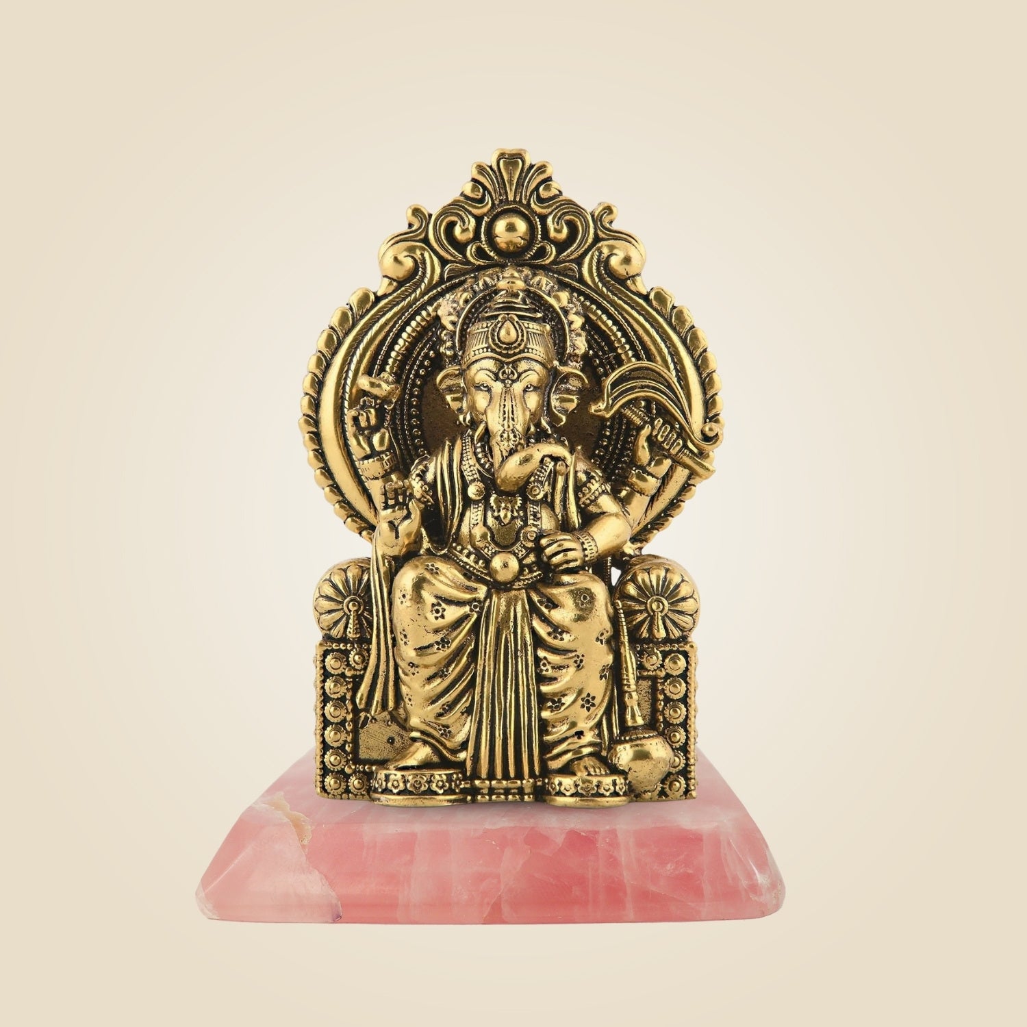 Gold-colored deity statue on a pink base against a beige background