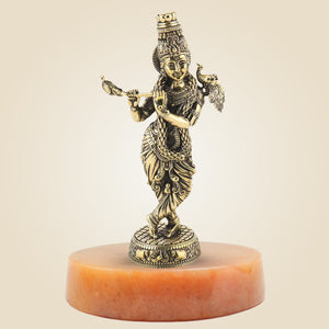 Bronze statue of a deity on a red stone base against a beige background