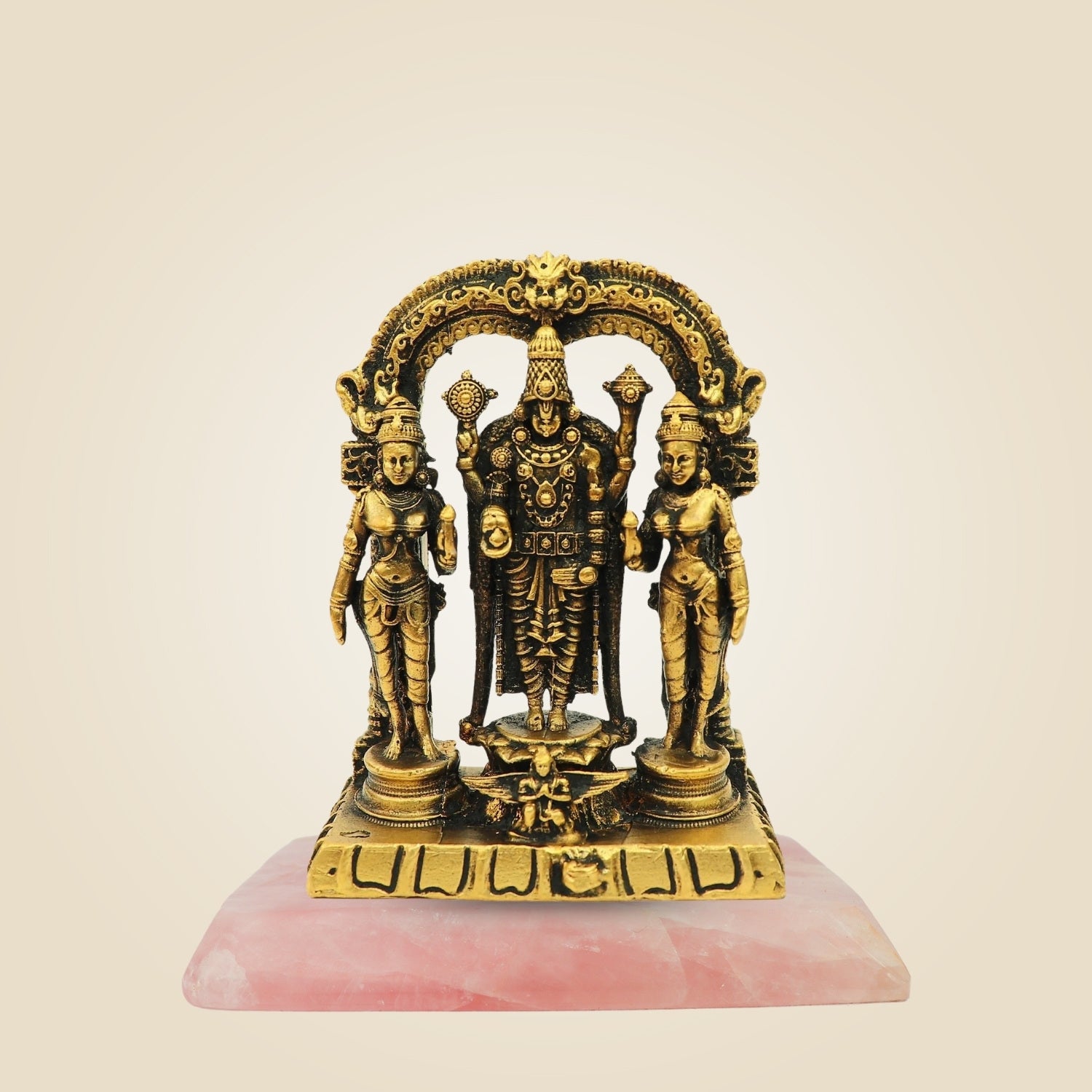 Gold-colored statue of three figures on a pink base against a beige background