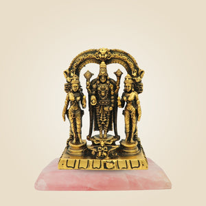 Gold-colored statue of three figures on a pink base against a beige background