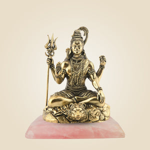Gold-colored statue of a seated figure with a trident on a pink base against a beige background
