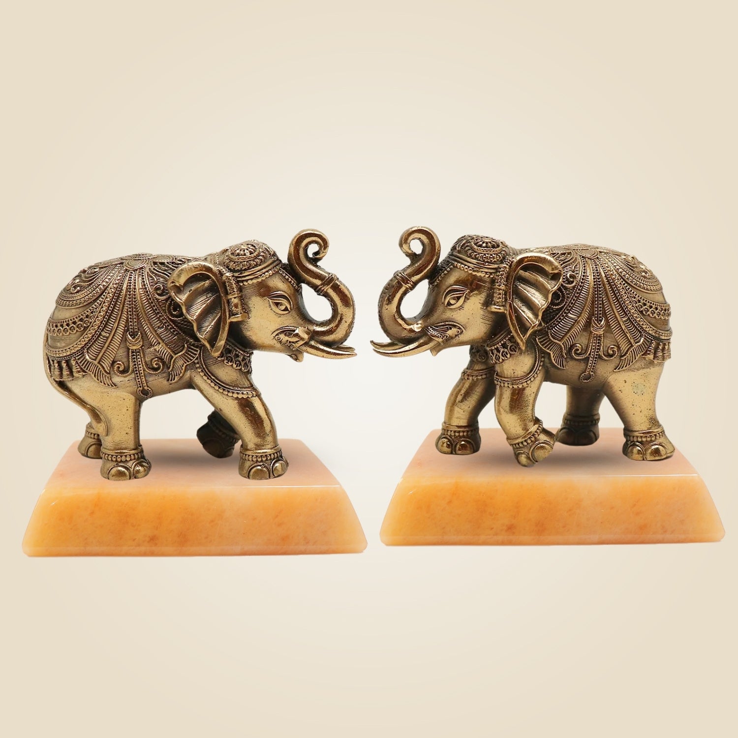 Two ornate brass elephant statues on a beige background