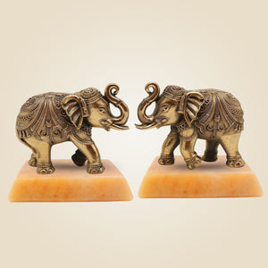 Two ornate brass elephant statues on a beige background