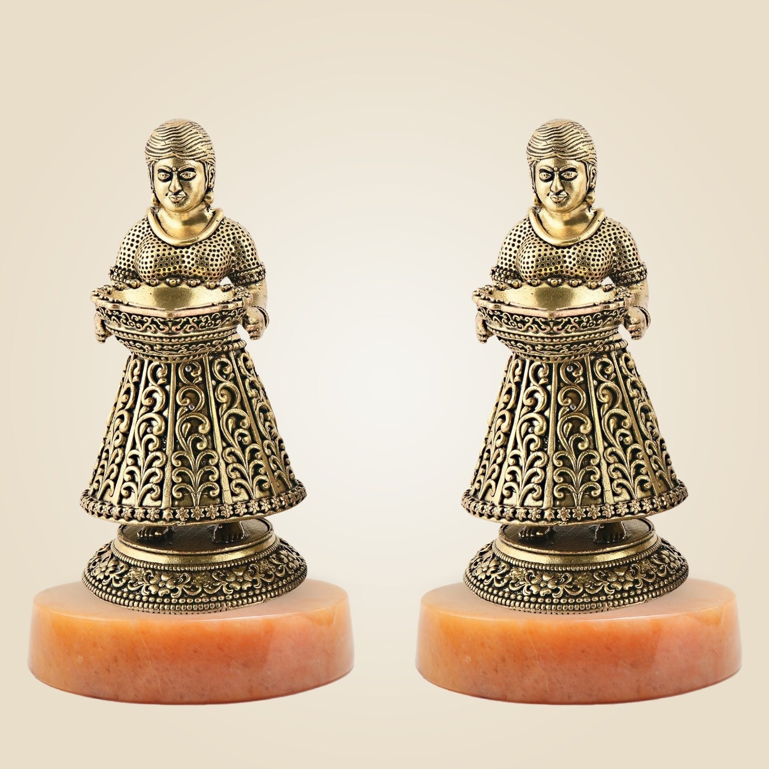 Two ornate figurines on pink bases against a beige background