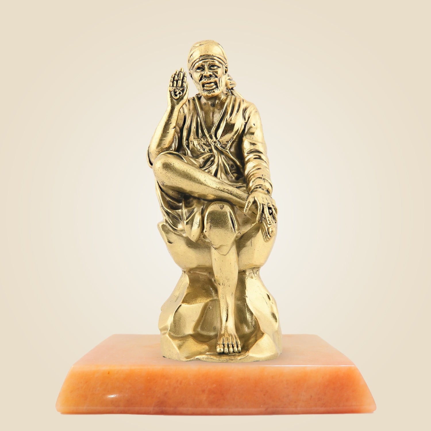 Gold statue of a seated figure on an orange base against a beige background