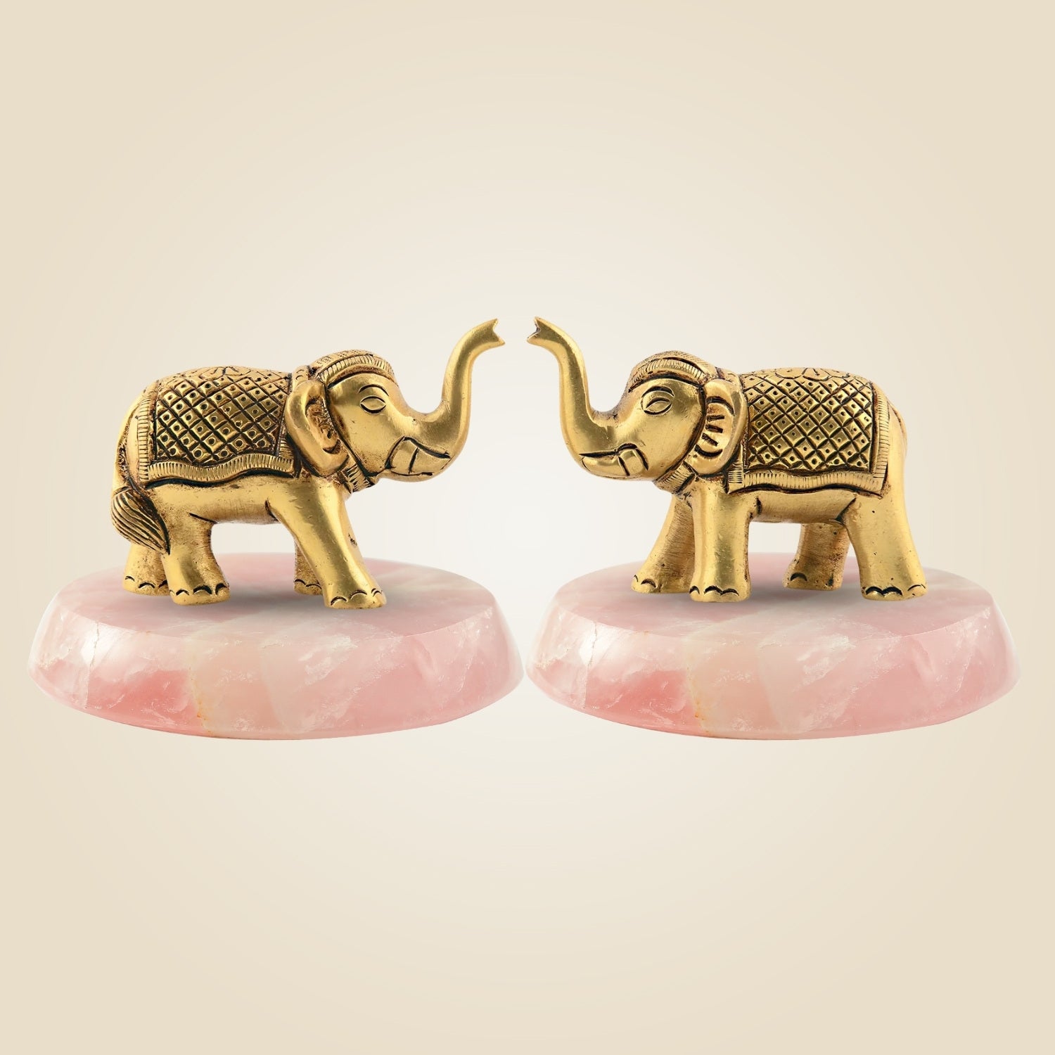 Two gold elephant figurines on pink bases against a beige background