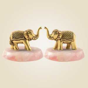 Two gold elephant figurines on pink bases against a beige background